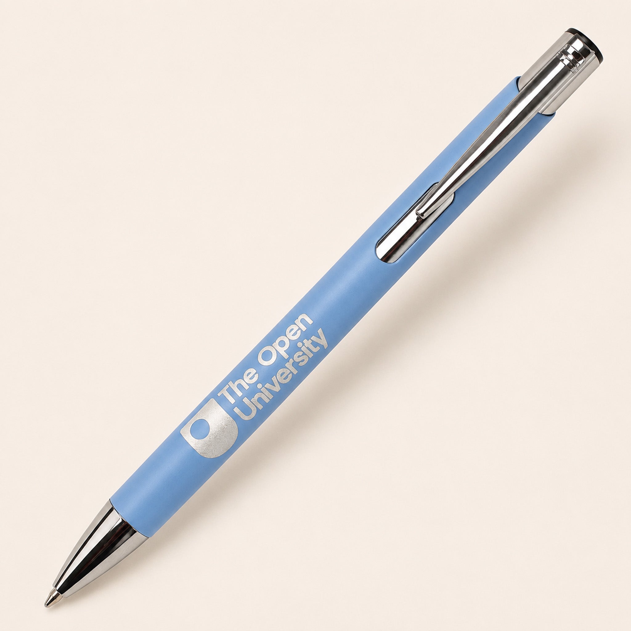 A light blue retractable pen with silver metal accents, featuring the text 'The Open University' printed in white on the barrel, set against a solid cream-colored background.
