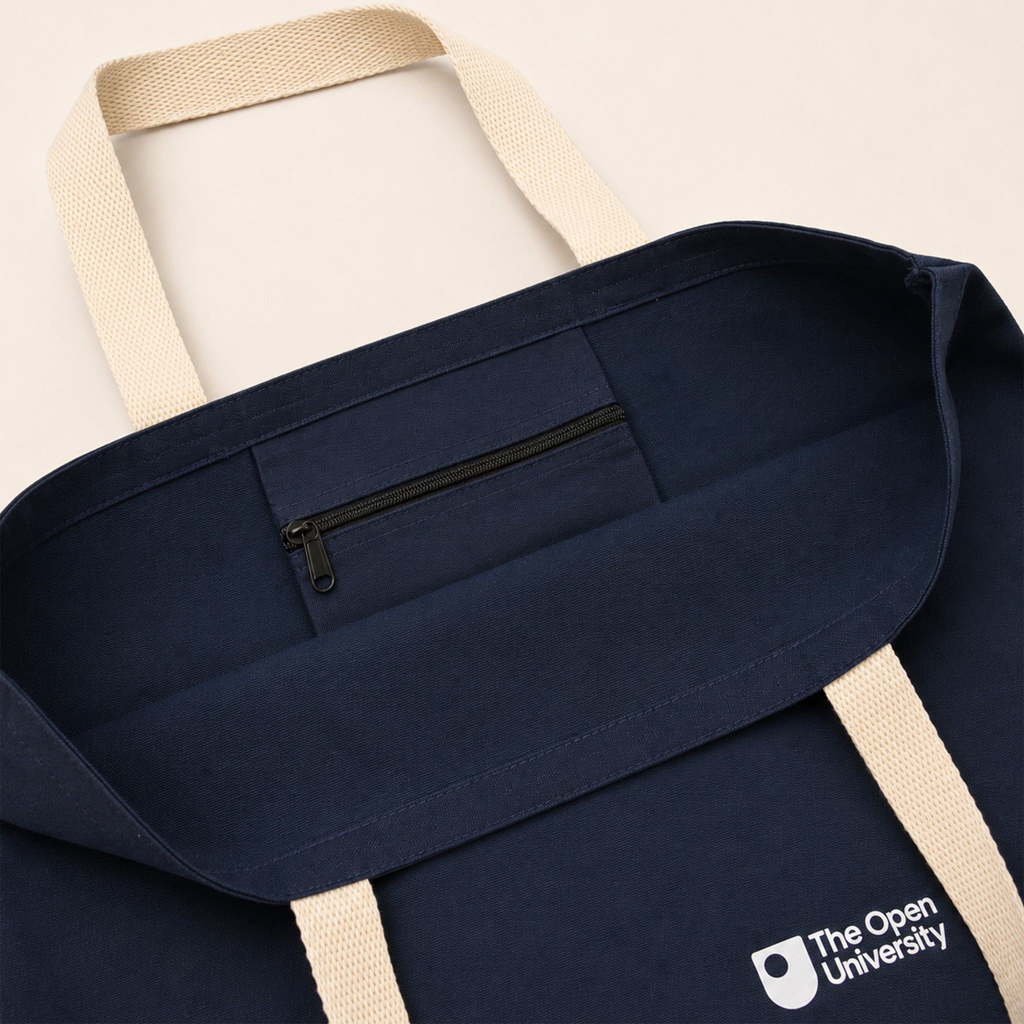 Close-up of a navy blue tote bag with cream-colored handles and a white printed logo for 'The Open University' in the bottom right corner.